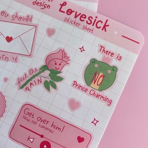 May include: A pink sticker sheet with a grid pattern. The sheet includes stickers with various designs, including a rose with a face, a frog with a crown, and a music player with the text "Get over him! Now, not tomorrow". The sheet also includes the text "Lovesick sticker sheet" and "There is no Prince Charming".