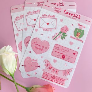 May include: A set of pink and white stickers with various designs and text. The stickers feature phrases like "Love is a disease", "Get over him!" and "Love is an illusion".