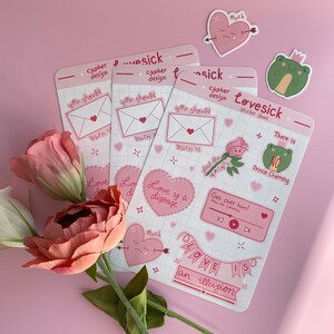 May include: A set of pink and white stickers with various designs, including hearts, flowers, frogs, and text. The text includes phrases like "Love is a disease", "Get over him!" and "Love is an illusion".