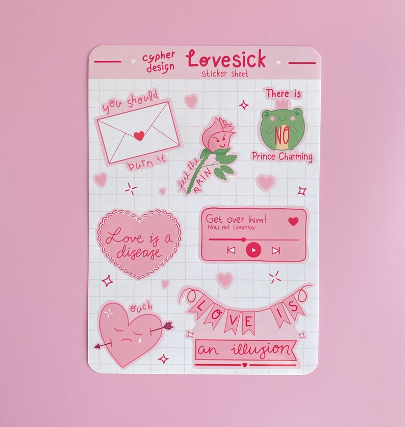 May include: A sheet of pink and white stickers with a love theme. The stickers feature illustrations of a heart with an arrow, a frog, a rose, a music player, and a banner that says "Love is an illusion".