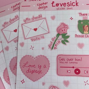 May include: A pink sticker sheet with various designs, including a heart with the text "Love is a disease", a rose with the text "Feel the pain", a frog with the text "No", and an envelope with the text "You should burn it".