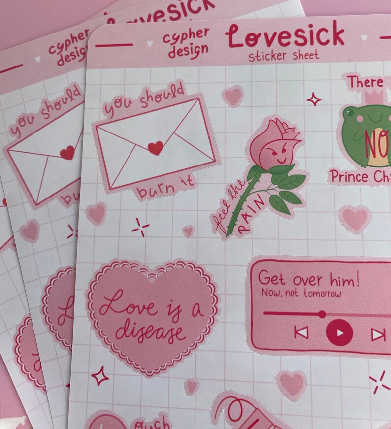 May include: A pink sticker sheet with various designs, including a heart with the text "Love is a disease", a rose with the text "Feel the pain", a frog with the text "No", and an envelope with the text "You should burn it".