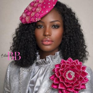 May include: A woman wearing a silver jacket with rhinestone trim and a pink flower brooch. She is also wearing a pink hat with floral and crystal embellishments. The image has the text "Bliss Beauty" in the lower left corner.
