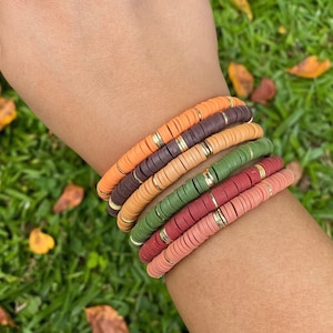 May include: A stack of colorful bracelets with gold accents. The bracelets are made of round beads in shades of orange, brown, green, and red.