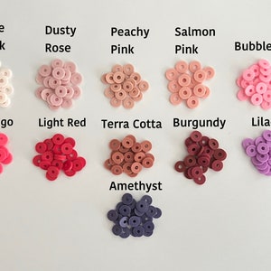 May include: Assortment of small, round, donut-shaped polymer clay beads in various shades of pink, red, and purple. The colors are labeled with names like "Pale Pink", "Dusty Rose", "Peachy Pink", "Salmon Pink", "Bubblegum", "Flamingo", "Light Red", "Terra Cotta", "Burgundy", "Lilac", and "Amethyst".