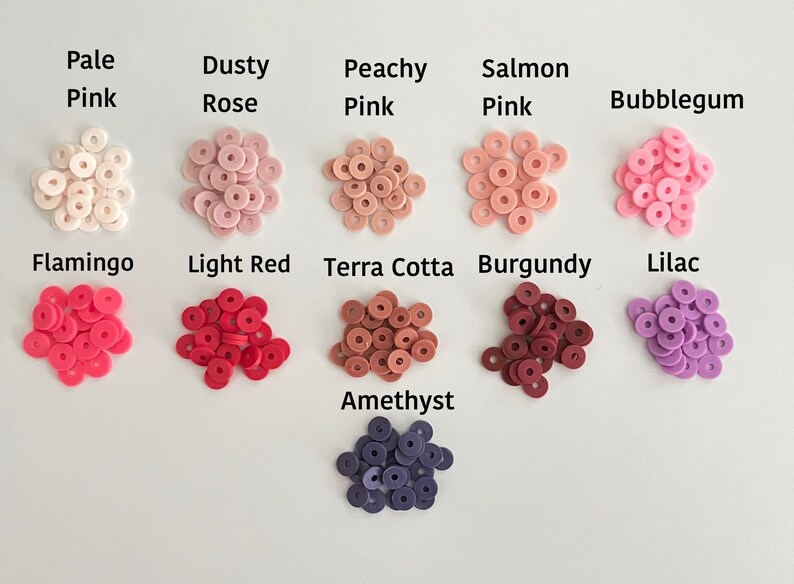 May include: Assortment of small, round, donut-shaped polymer clay beads in various shades of pink, red, and purple. The colors are labeled with names like "Pale Pink", "Dusty Rose", "Peachy Pink", "Salmon Pink", "Bubblegum", "Flamingo", "Light Red", "Terra Cotta", "Burgundy", "Lilac", and "Amethyst".
