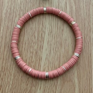 May include: A pink and silver beaded bracelet with a round shape.