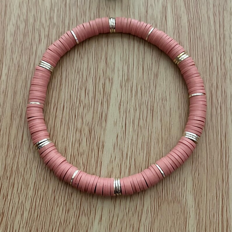 May include: A pink and silver beaded bracelet with a round shape.