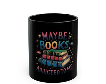 Puede incluir: Taza de cerámica negra con el texto "MAYBE BOOKS ADDICTED TO ME" y un gráfico de tres libros apilados. Los libros son verdes, rojos y azules. El texto está en una fuente colorida y caprichosa con acentos de estrellas.