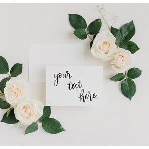 May include: White stationery set with a blank card and envelope, adorned with cream-colored roses and green leaves. The card features the text "your text here" in elegant script, perfect for invitations or notes.