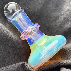 May include: A colorful glass pipe with a rounded end and a clear, spherical top. The pipe features a blend of blue, green, and orange hues, with a clear, iridescent finish. The design includes a bulbous base and a cylindrical stem.