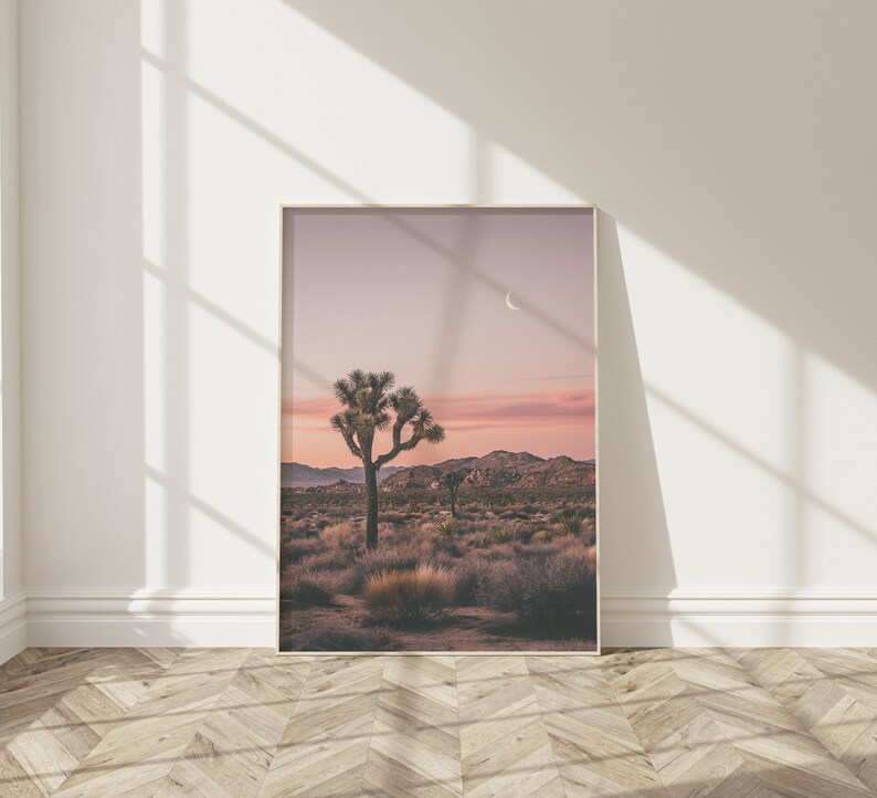May include: A framed photograph of a desert landscape with a single Joshua tree in the foreground. The sky is a soft pink and purple, with a crescent moon visible in the upper right corner.