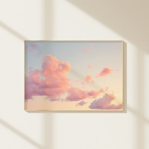 May include: A framed photograph of a pink and blue sunset sky with fluffy clouds. The clouds are a soft pink and white, and the sky is a light blue with a hint of orange.