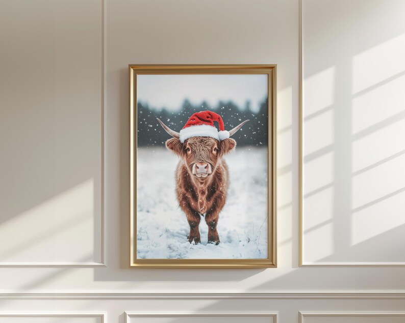 May include: A framed print featuring a Highland cow wearing a red and white Santa hat, standing in the snow. The cow has long, shaggy brown fur and curved horns. The background shows a snowy landscape with trees.