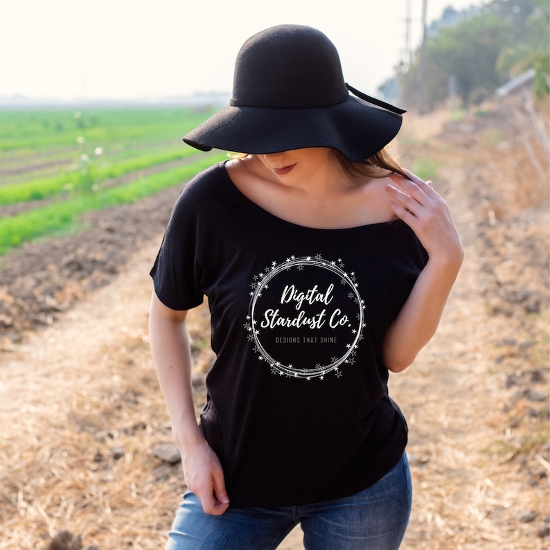 May include: A black off-the-shoulder t-shirt with a white graphic design of a circle with snowflakes and the text "Digital Stardust Co. Designs that shine".