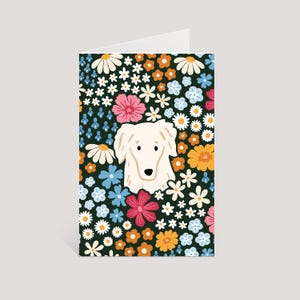 May include: A folded greeting card featuring a central illustration of a cream-colored dog head surrounded by a dense pattern of colorful flowers including white daisies, orange blossoms, pink petals, and light blue blooms on a dark green background.
