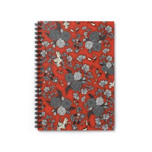 Puede incluir: Un cuaderno de espiral con un fondo rojo vibrante y un patrón repetitivo de ilustraciones florales grises y blancas, zapatos de tacón alto, barras de labios y pequeños motivos de mariquitas dispersos por toda la cubierta frontal.