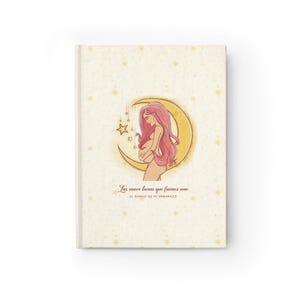 Puede incluir: Un diario de tapa dura color crema con un patrón de pequeñas estrellas doradas. La ilustración central muestra a una persona embarazada con largo cabello rosa frente a una gran luna creciente amarilla. Texto: Las nueve lunas que fuimos uno EL DIARIO DE MI EMBARAZO.