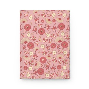 Puede incluir: Un cuaderno rectangular con una cubierta de color rosa polvoriento que presenta un patrón repetitivo de botellas de vino, copas, zapatos de tacón, abanicos, discos de vinilo y frascos de perfume en tonos crema, rosa claro y marrón rojizo.