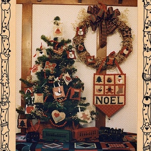 Pode incluir: Um livreto de padrões de artesanato vintage que apresenta uma árvore de Natal decorada com ornamentos feitos à mão. A capa apresenta uma fita de xadrez vermelho e verde, uma coroa e uma faixa que diz "NOEL". O título do padrão é "PENSTITCH ORNAMENTS" e a parte inferior da capa diz "MUMM'S THE WORD".