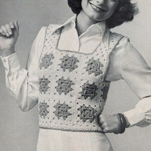May include: A woman wearing a white blouse and a crocheted vest with a square pattern. The vest is white with brown accents. She is wearing a white skirt and has her hair styled in a short, curly bob.