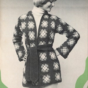 May include: A black and white crocheted cardigan with a square pattern and a matching belt. The cardigan is open in the front and has long sleeves.