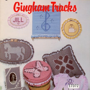 May include: A collection of gingham fabric crafts, including a cushion with a flower design, a butterfly-shaped lid for a jar, a framed picture, and a small cushion with a flower design. The crafts are all made with gingham fabric in various colours, including red, white, blue, pink, and brown.