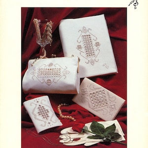 May include: An image of a collection of white Hardanger embroidery items, including a clutch, a small purse, a book cover, and a small case. The items are displayed on a red background with a rose, gloves, and a glass with pearls. The text "Hardanger Elegance" is at the top.