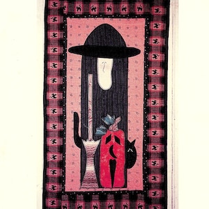 May include: A black and red quilted wall hanging with a witch, a broom, a pumpkin, and a black cat. The background is a pink and white plaid pattern.