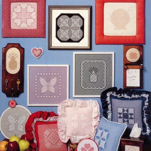 May include: An assortment of chicken scratch embroidery items, including framed pictures and cushions. Designs feature geometric shapes, butterflies, and flowers. The colour scheme includes red, pink, blue, and white. A wooden key holder and small wooden box are also visible.