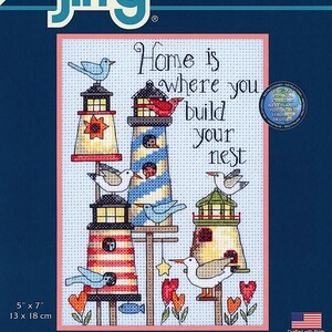 May include: A counted cross stitch kit featuring a colorful illustration of lighthouses with birds and the text "Home is where you build your nest". The kit includes 14 count light blue Aida fabric, cotton thread, a needle, and easy instructions. The kit is 5 inches by 7 inches or 13 centimeters by 18 centimeters.