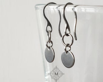 May include: A pair of silver dangle earrings with small round discs hanging from the bottom. The earrings have a simple, minimalist design.