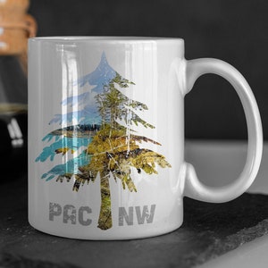 May include: White ceramic mug with a graphic of a tree with a blue, green, and brown color scheme. The text "PAC NW" is printed on the mug.