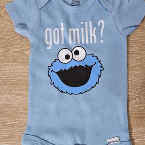 May include: Light blue baby onesie with the text "got milk?" above a cartoon Cookie Monster face. The onesie has short sleeves and snap closures at the bottom. The brand name "Gerber" is visible.