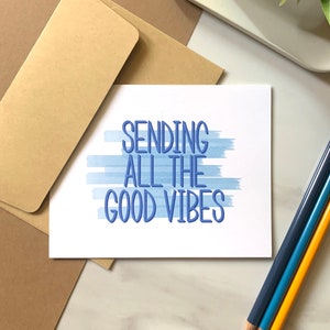 May include: A white card with blue watercolor stripes and the text "Sending all the good vibes" in blue lettering.