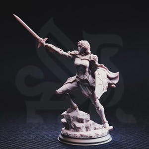 Puede incluir: Figura detallada de una mujer guerrera en una pose dinámica, sosteniendo una espada y un escudo. La figura está vestida con armadura y se encuentra sobre una base rocosa. El color es un tono monocromático apagado, con detalles intrincados.