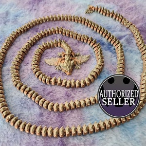 May include: A coiled, segmented, spiky, brown and tan colored chain with a small, spiky, brown and tan colored lizard figurine in the center. The chain and figurine are on a fuzzy, purple and blue background. The text "AUTHORIZED SELLER" is on a black circle with a purple background.