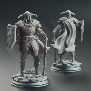 Puede incluir: Una detallada figura de un guerrero con armadura completa, sosteniendo una espada y un escudo. La figura tiene un casco con cuernos y una capa fluida. La armadura está intrincadamente diseñada, y la figura se encuentra sobre una base con detalles de piedra. Una segunda figura es visible en el fondo.