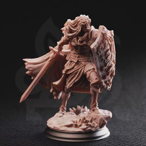 Puede incluir: Figura detallada de un guerrero en pose dinámica, empuñando una espada y un escudo. La figura está vestida con armadura y una capa fluida, de pie sobre una base rocosa. El escudo presenta un diseño ornamentado, y el color general es un tono apagado y terroso.