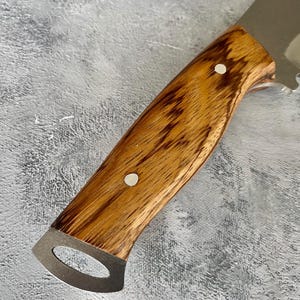 K&ouml;nnte beinhalten: Ein Messer mit einem Holzgriff und einer Klinge aus Edelstahl. Der Griff ist aus dunklem Holz mit einer hellbraunen Maserung. Am Griff befinden sich zwei silberne Nieten.