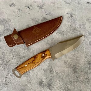 K&ouml;nnte beinhalten: Eine braune Ledertasche f&uuml;r ein Messer mit einem dekorativen Design und ein Messer mit Holzgriff und silberner Klinge.