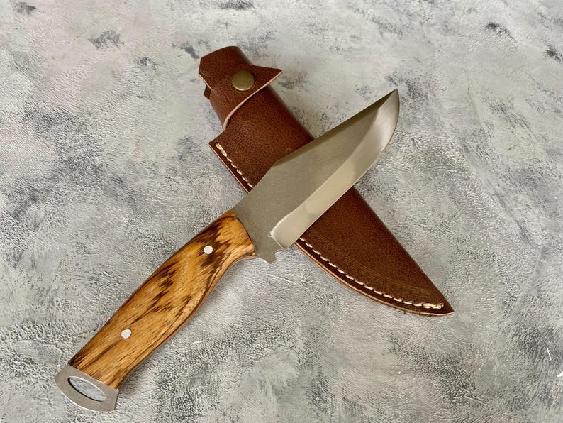 K&ouml;nnte beinhalten: Ein Jagdmesser mit silberner Klinge und einem Holzgriff in einer braunen Lederscheide mit Naht.