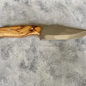 K&ouml;nnte beinhalten: Ein Messer mit braunem Holzgriff und silberner Klinge. Das Messer liegt auf einer grauen, strukturierten Oberfl&auml;che.
