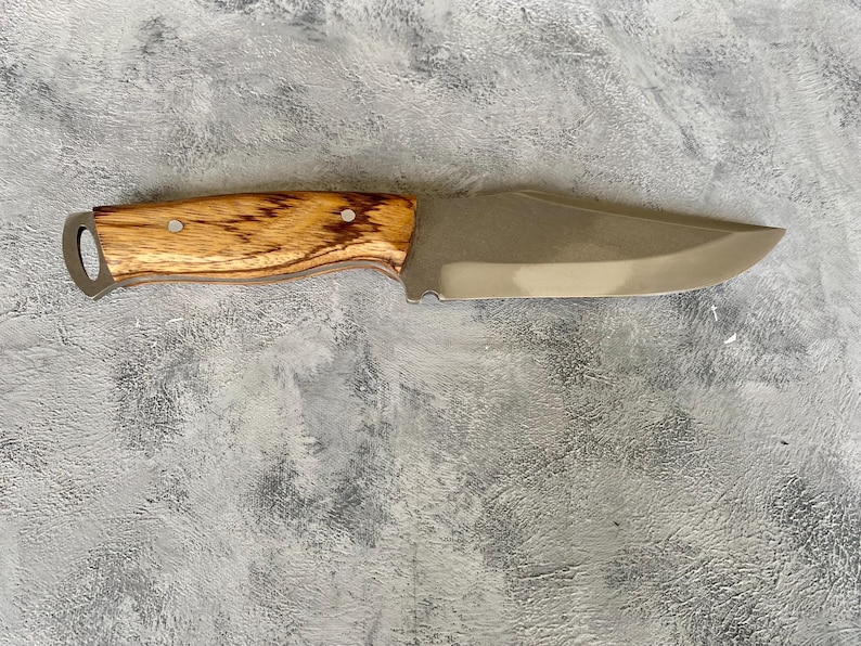 K&ouml;nnte beinhalten: Ein Messer mit braunem Holzgriff und silberner Klinge. Das Messer liegt auf einer grauen, strukturierten Oberfl&auml;che.