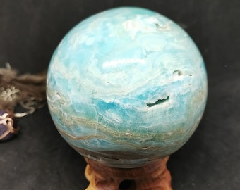 May include: A blue and green celestite sphere on a wooden stand. The sphere has a swirling pattern of blue and green.