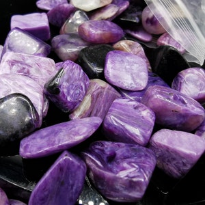 May include: A collection of purple and black tumbled stones. The stones are smooth and polished, with a variety of patterns and swirls.