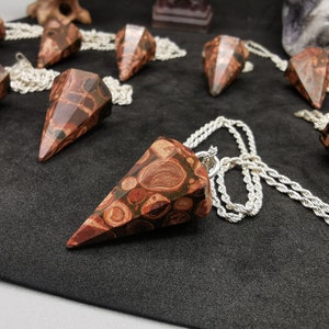May include: A collection of brown and red jasper stone pendants with silver chains. The pendants are shaped like a point and have a swirling pattern.