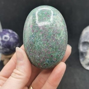 May include: An oval-shaped gemstone with a smooth, polished surface. The gemstone is green with small, red inclusions.