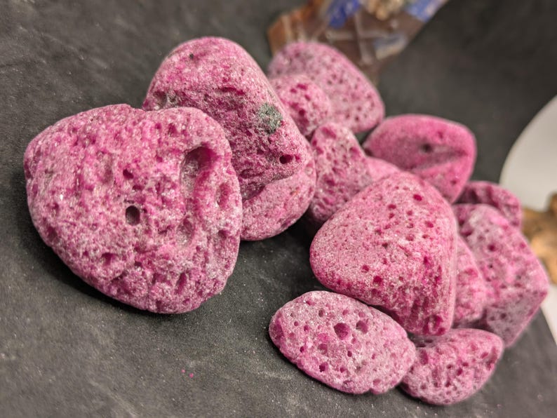 May include: A cluster of irregularly shaped, porous, pink rocks. The rocks have a rough, textured surface with numerous small holes. The color is a vibrant, saturated pink, and they appear to be natural formations.