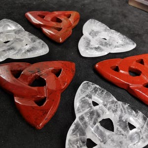 May include: Five Celtic knot triquetra pendants, two are made of clear quartz and three are made of red jasper.